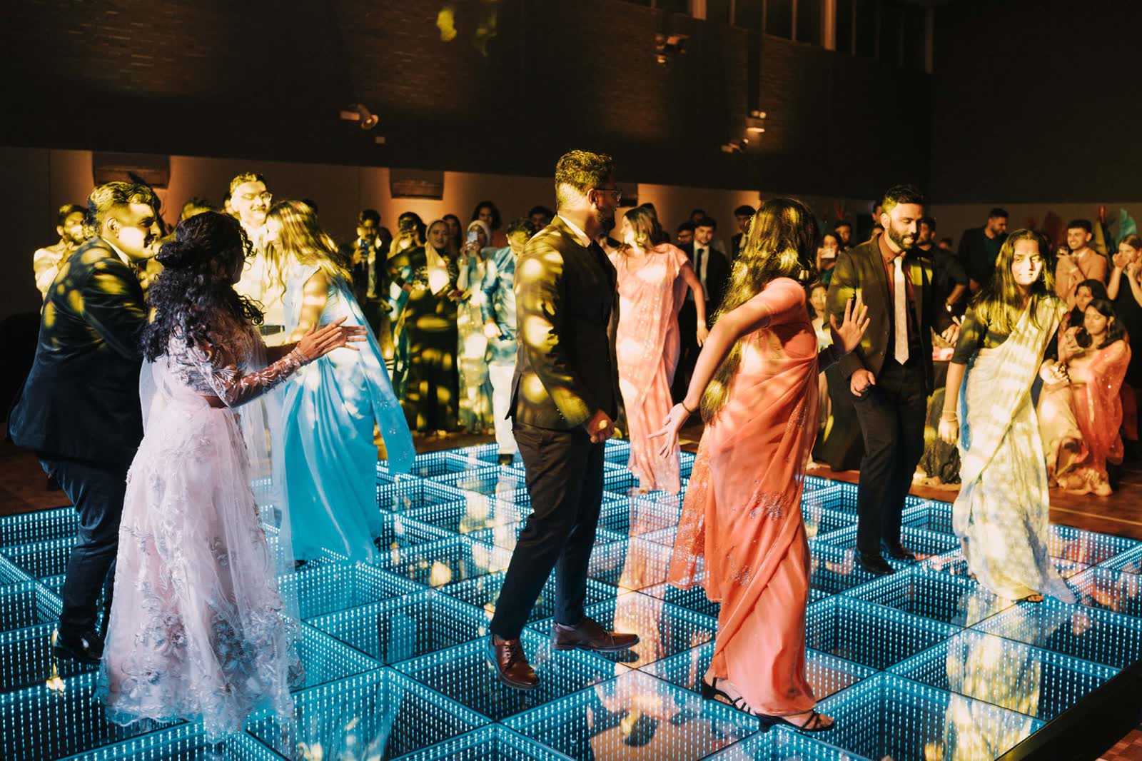 A packed 3D infinity LED dance floor glowing blue and green at a Perth celebration